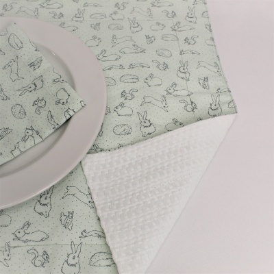 Guardanapo e toalha de mesa branco com desenhos cinzentos de coelhos e alimentos, prato branco