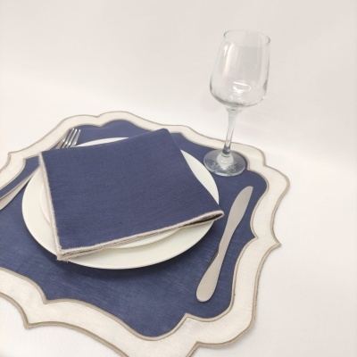 Conjunto de loiça com prato branco, guardanapo azul, base para prato azul e bege, talheres metálicos e copo de vidro