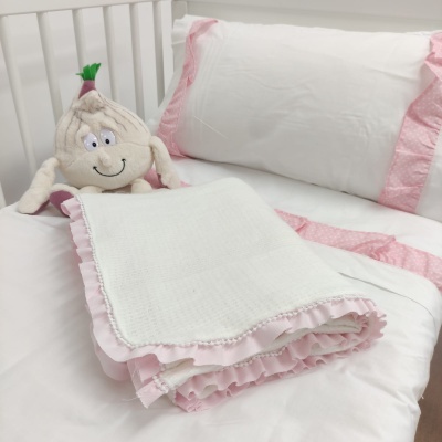 Lençóis de cama brancos com franjas rosas, manta branca com babados rosa e boneco de pelúcia de alho.