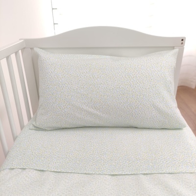 Lençol e fronha de bebé com padrão floral sobre cama branca de berço