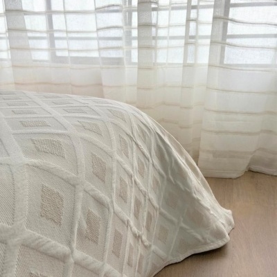 Cobertura de cama branca com padrão geométrico 3D, cortinas brancas e chão de madeira