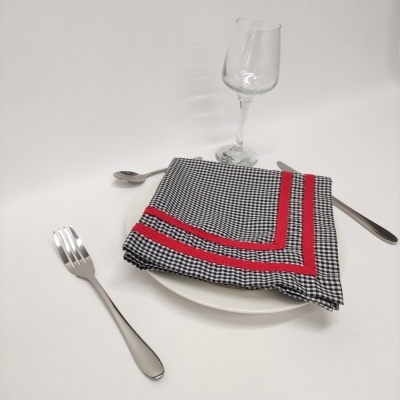 guardanapo de tecido pied-de-poule com riscas vermelhas sobre prato branco, talheres e taça