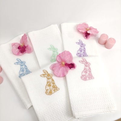 Toalhas brancas com bordado de coelhos coloridos, flores cor-de-rosa e velas rosas ao redor