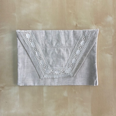 Guardanapo cinza claro com renda branca em forma de V sobre fundo bege.