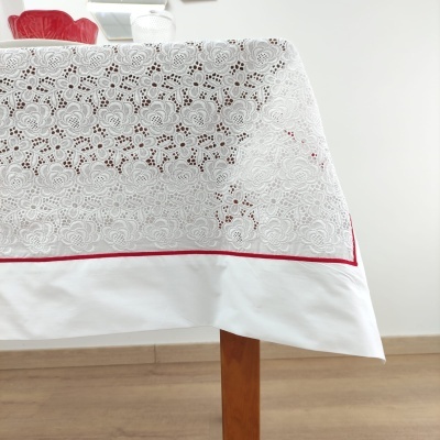 Toalha de mesa branca com bordado floral e borda vermelha sobre mesa de madeira