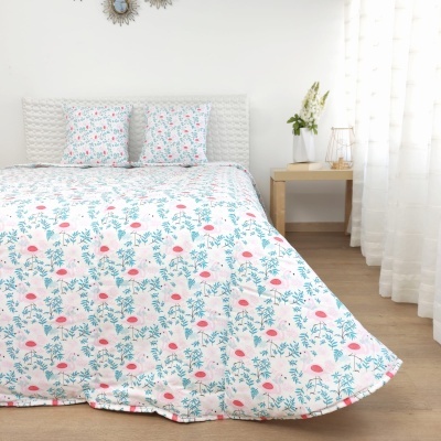 Colcha e almofadas florais em quarto com cabeceira branca e mesa de madeira