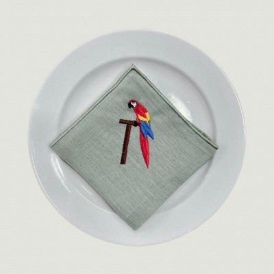 Guardanapo cinza claro com bordado de papagaio sobre prato branco
