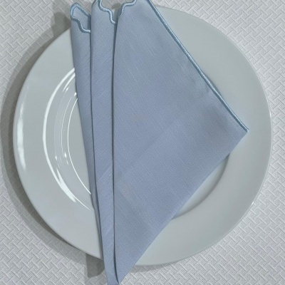 Guardanapo azul claro dobrado sobre prato branco num fundo branco com padrão geométrico