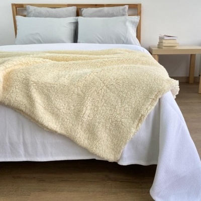 Cama arrumada com manta creme felpuda e mesa de madeira com livros