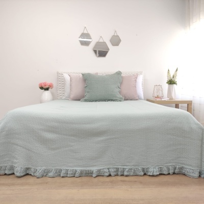 Cama com colcha verde água e almofadas, em ambiente claro com espelhos na parede.