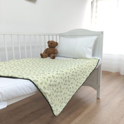 Cama de criança branca com manta amarela de padrão floral e ursinho de peluche castanho