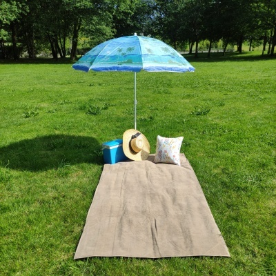 Conjunto de piquenique com toalha bege, almofada, chapéu de palha, cooler azul e guarda-sol azul num parque