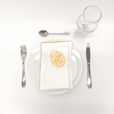 Mesa posta com prato branco, talheres de metal, toalhete bordado e copo de vidro