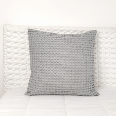 Almofada cinzenta texturada sobre cama branca acolchoada