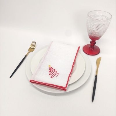 Conjunto de prato branco com guardanapo bordado, talheres dourados e pretos e copo de vidro vermelho