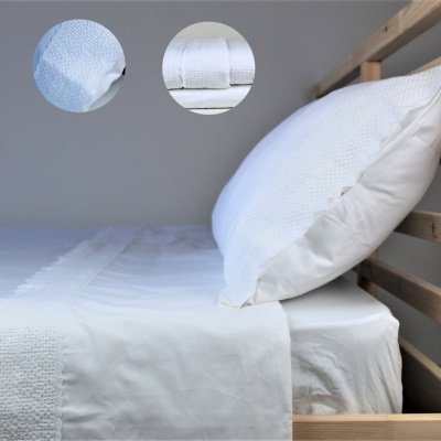 Cama de madeira clara com lençóis e fronhas brancas texturizadas