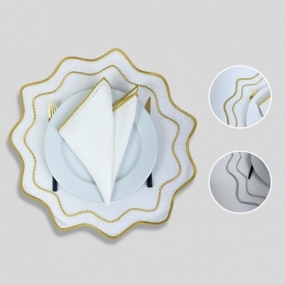 Guardanapos e sousplats brancos com bordas douradas onduladas sobre prato branco