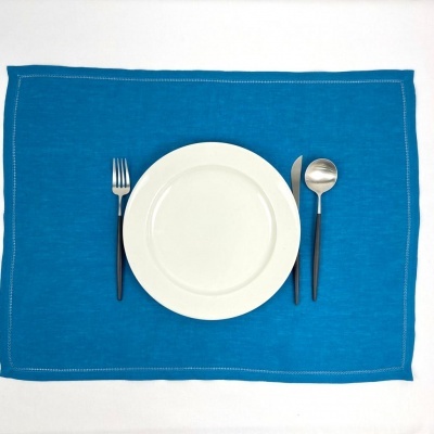 Conjunto de jantar com prato branco e talheres com cabos pretos sobre placemat azul