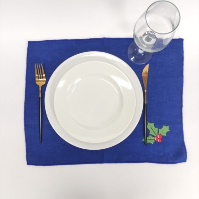Mesa posta com individual azul, prato branco, talheres dourados e copo de vidro