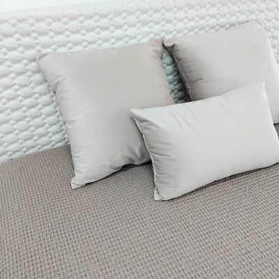 Conjunto de almofadas cinza claro sobre manta cinza e fundo branco acolchoado