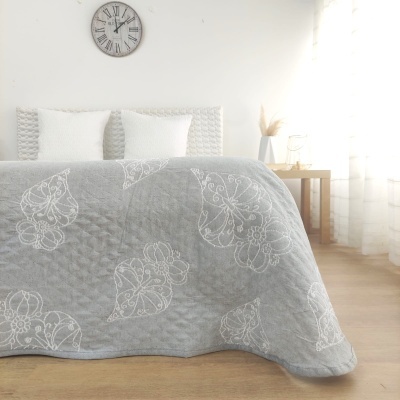 Cobertura de cama cinzenta com padrão de folhas brancas e almofadas brancas num quarto claro