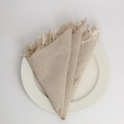 Guardanapo bege claro com franjas dobrado num prato branco