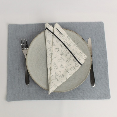 Conjunto de prato, guardanapo e talheres sobre individual cinza azulado