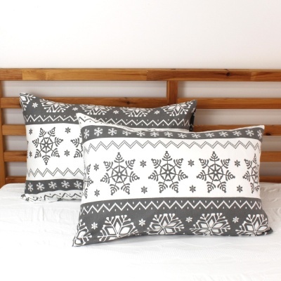 Almofadas retangulares cinza e branco com padrão de flocos de neve numa cama com cabeceira de madeira.