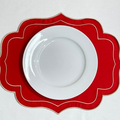 Prato branco de cerâmica sobre jogo americano vermelho com bordas douradas