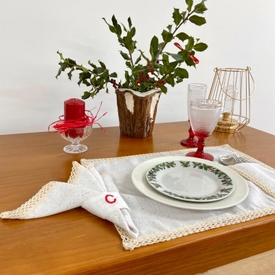 Conjunto de jantar sobre mesa com pratos, copos, guardanapo, vela e vaso decorativo com planta