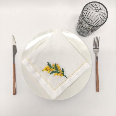 Conjunto de mesa com prato branco, guardanapo bordado, talheres com cabo de madeira e copo de vidro