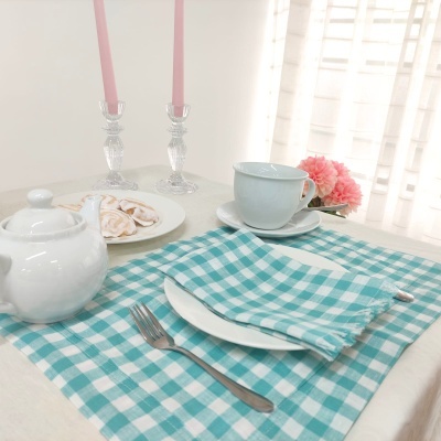 Mesa posta com toalha xadrez azul e branco, louça branca e velas rosas