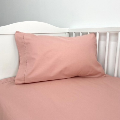 Almofada e lençol rosa numa cama branca infantil