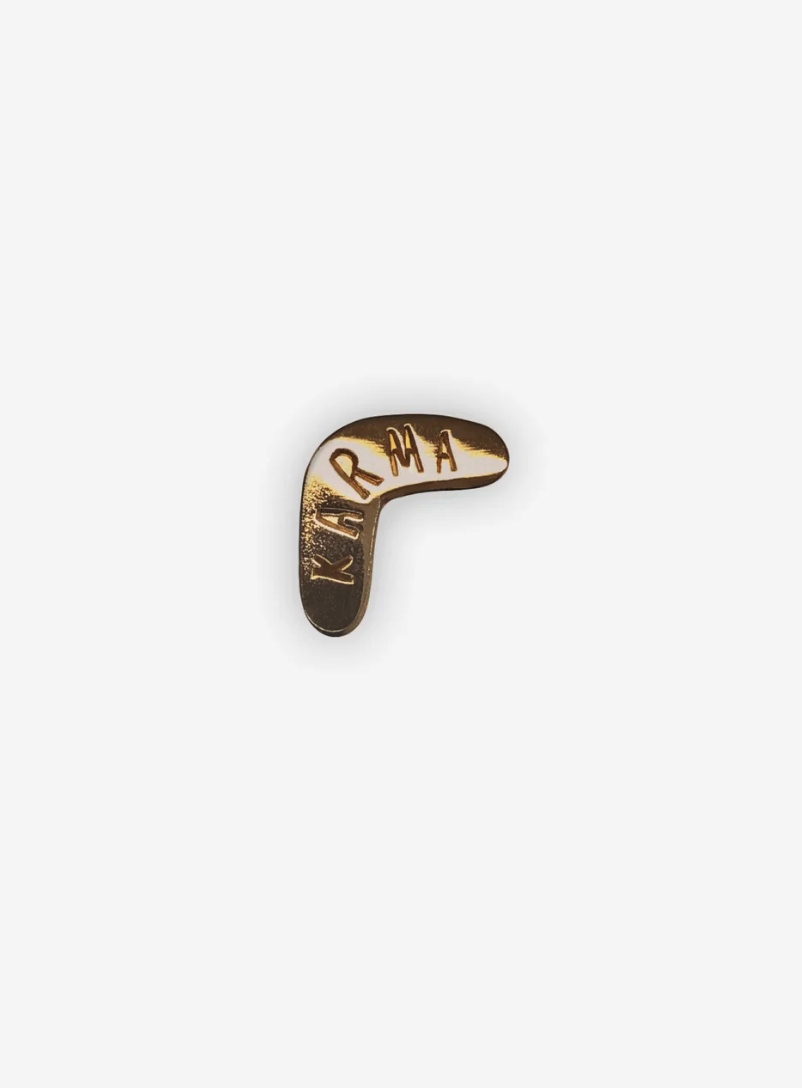 PIN "KARMA" TYPEALIVE Botão dourado em forma de bumerangue com a palavra KARMA