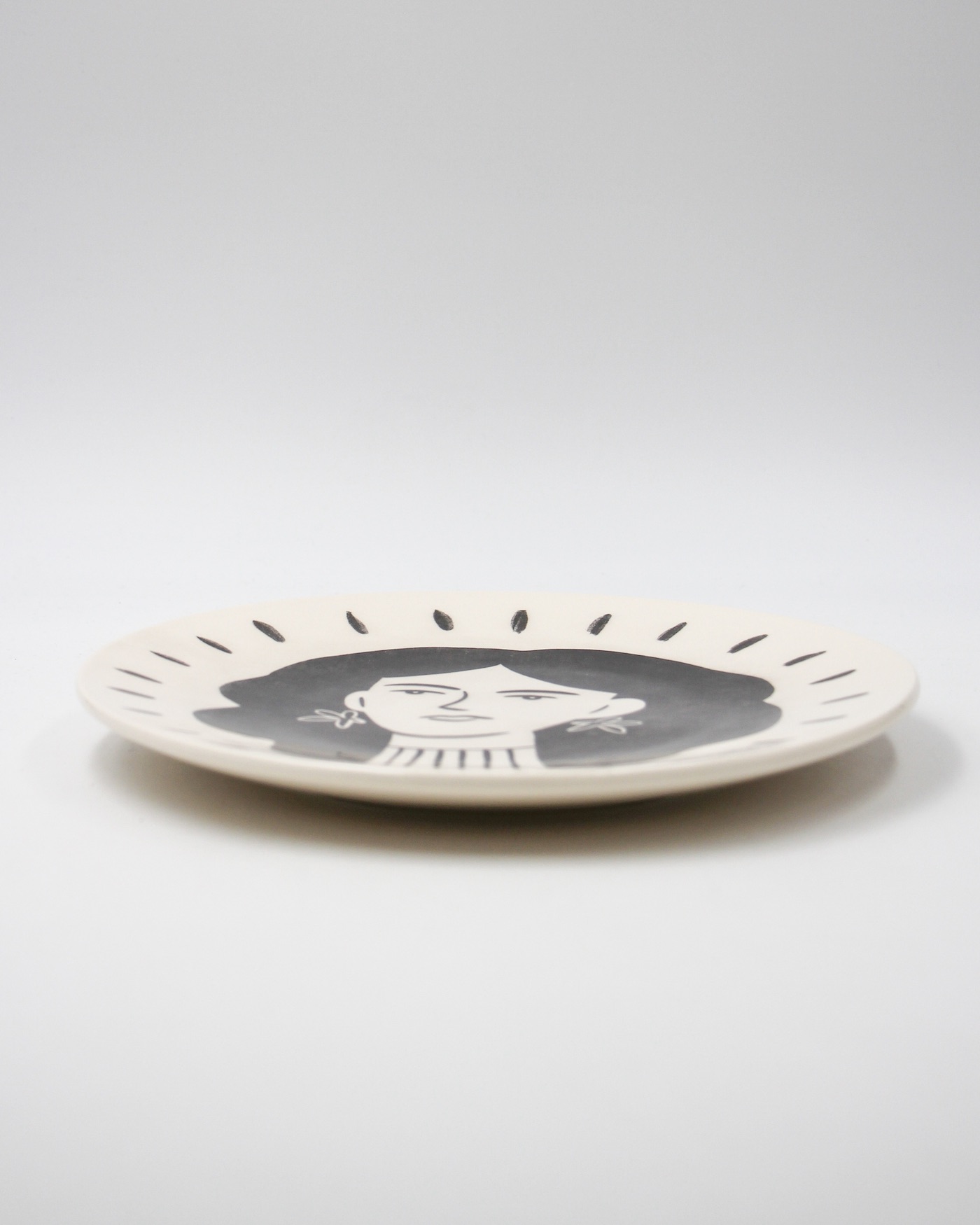 PRATO ILUSTRADO "MULHER" BÁRBARA AMARAL E PÓ DE BARRO Prato cerâmico bege com desenho de rosto feminino a preto