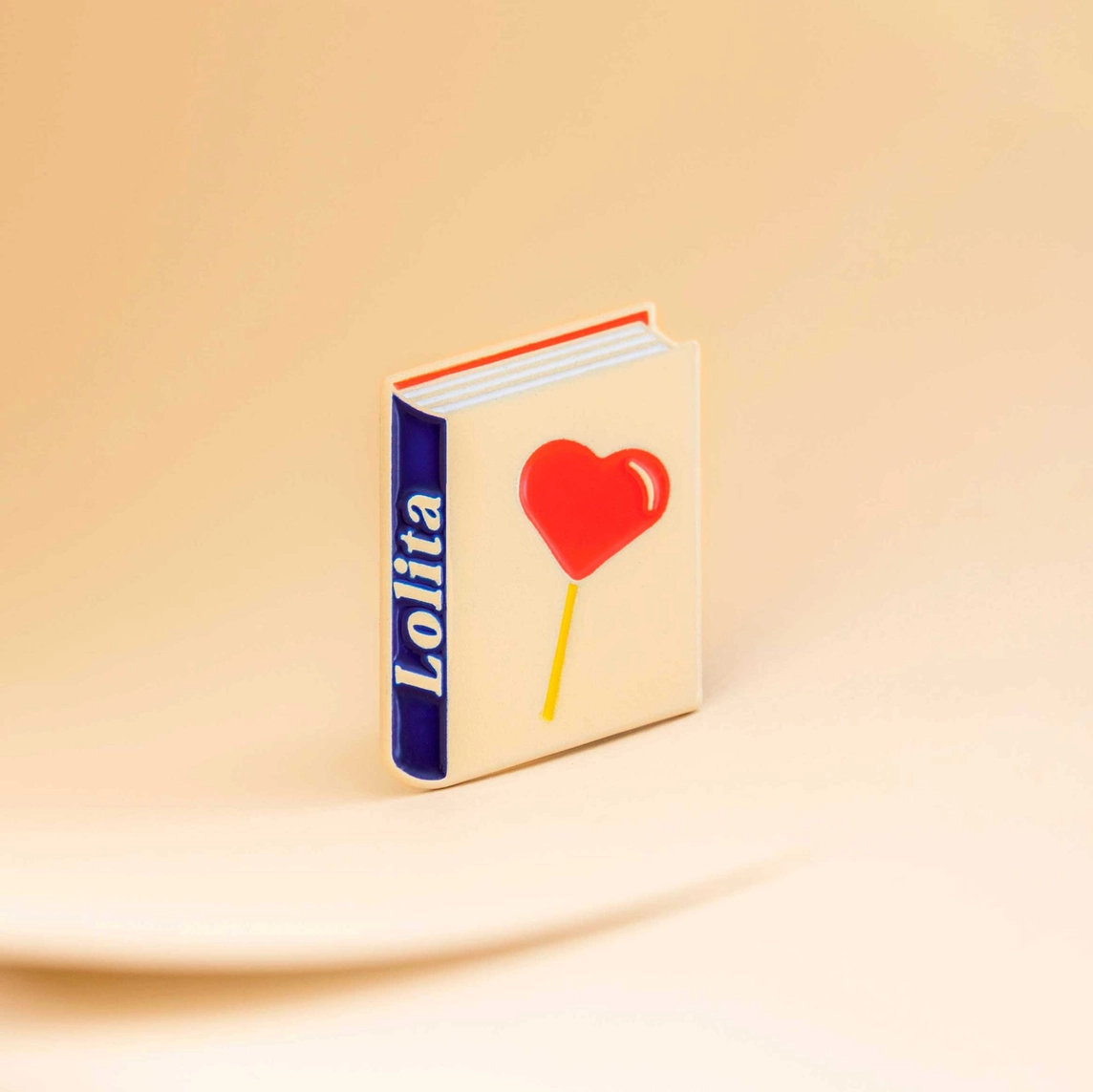 PIN "LOLITA BY VLADIMIR NABOKOV" JUDY KAUFMANN Livro com capa branca e pirulito em forma de coração