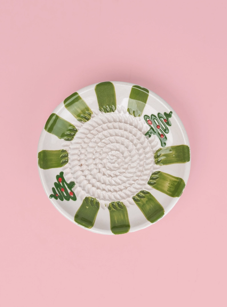 PRATO RALADOR PEQUENO "VERDE PERENE" ALFAR TIERRA COCIDA Prato cerâmico redondo branco com faixas verdes e árvores de Natal, fundo rosa.