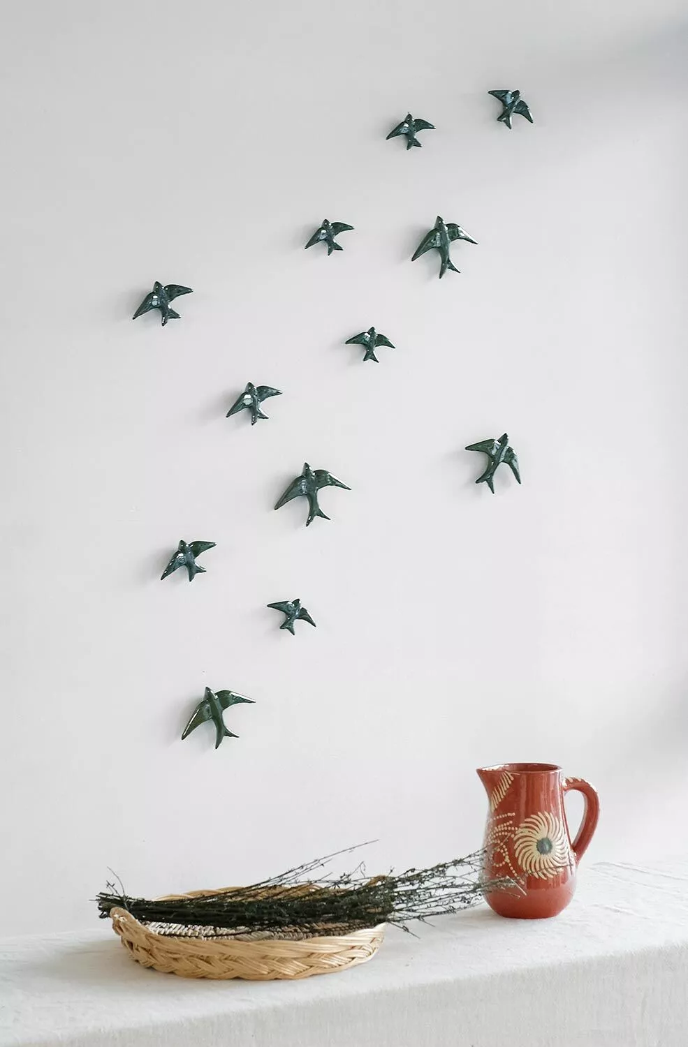 GLAZED OLIVE SWALLOW CASA ATLANTICA Decoração de parede com pássaros metálicos e jarro de cerâmica sobre mesa