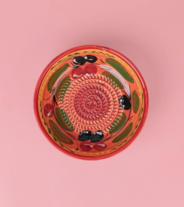 TAÇA RALADOR MÉDIO "PROVENÇAL" ALFAR TIERRA COCIDA Prato raso em cerâmica pintado com padrão de azeitonas e cerejas sobre fundo rosa.