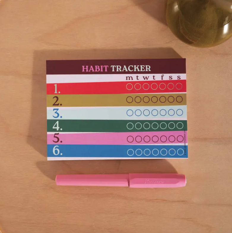 BLOCO DE NOTAS SEMANAL "HABIT TRACKER" - GOOD TUESDAY Habit Tracker colorido com caneta rosa sobre mesa de madeira clara