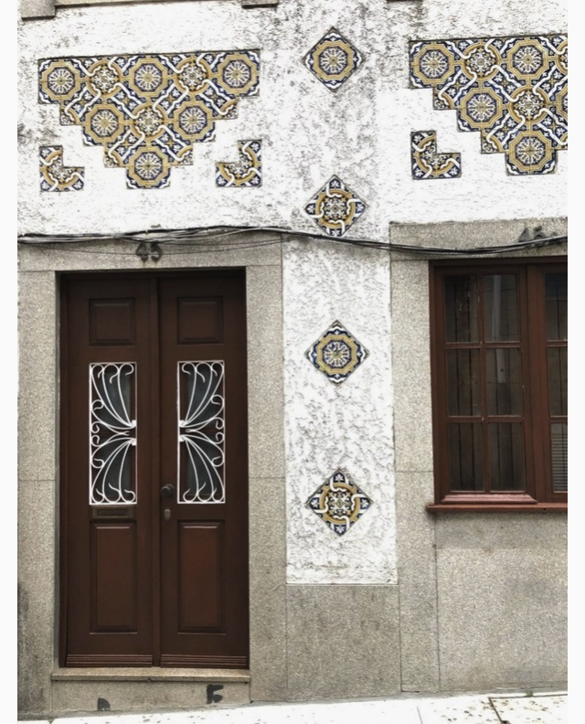 "AZULEJO PORTUGUÊS - CEDOFEITA" - UNWIND STUDIO Porta dupla de madeira com grades brancas e azulejos decorativos numa parede de pedra