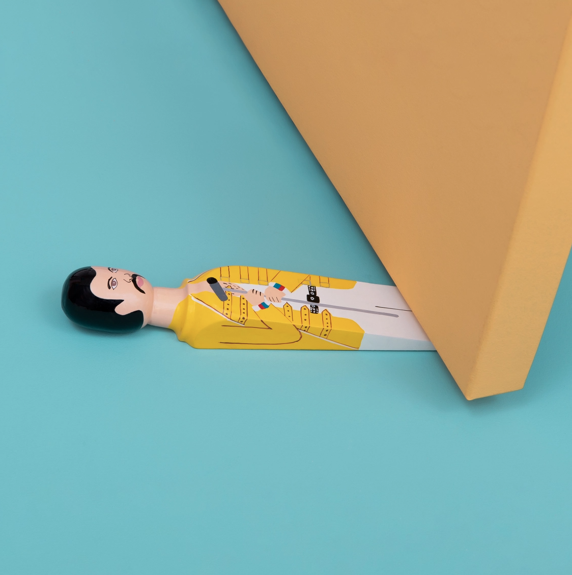 Door Stopper - Freddie Mercury (Freddy) WEDGIE Restritor de porta de madeira pintado com figura masculina, sob porta amarela, em superfície azul.