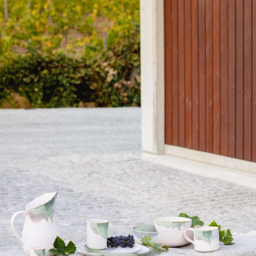 CANECA DOURO EGG BACK HOME Conjunto de louça cerâmica branca com padrão verde, folhas e uvas, em ambiente exterior