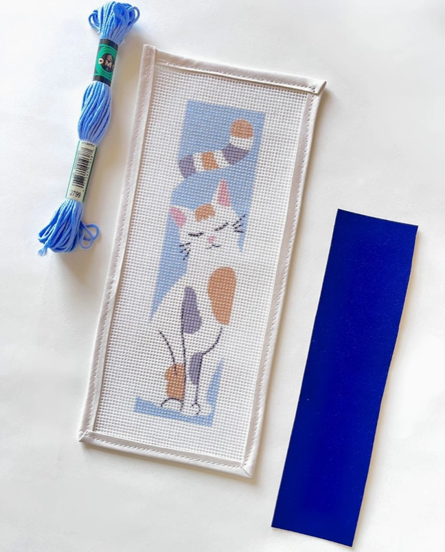 "THE GREAT CATSBY BOOKMARK NEEDLE STICH KIT " UNWIND STUDIO Kit de ponto cruz com gato bordado, fio azul claro e faixa de tecido azul escuro.