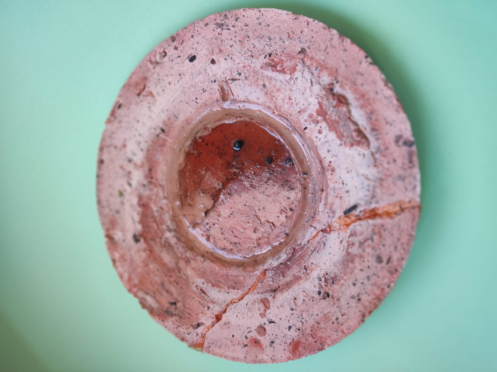 PRATO REDONDO PARA SERICAIA "TABLEWARE FOR ISOLATION" MARQUES MARQUES Prato redondo rosa de cerâmica com fissuras sobre fundo verde claro