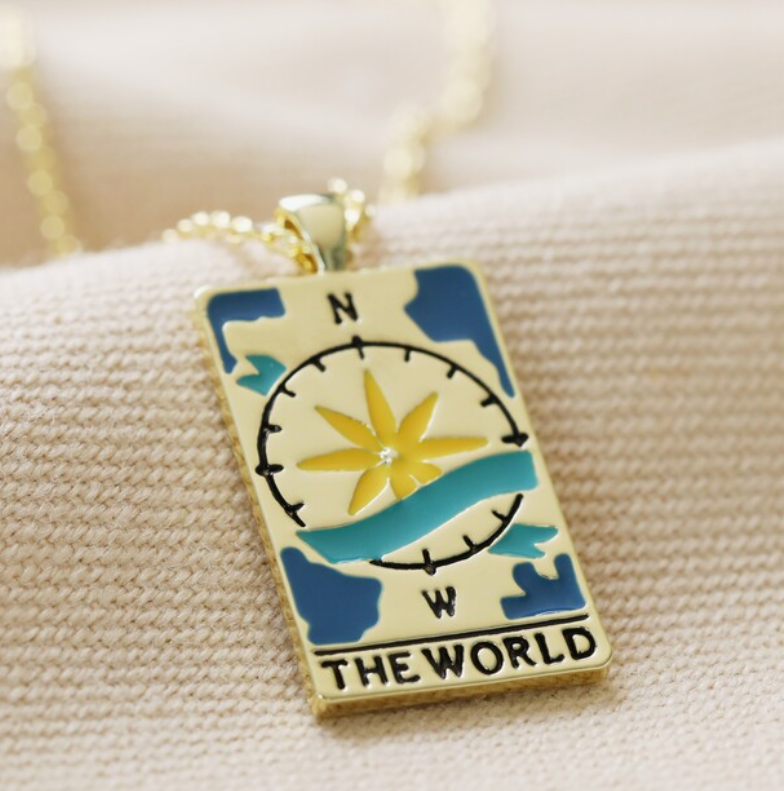 COLAR DOURADO "THE WORLD" LISA ANGEL Pendente dourado com desenho azul e amarelo de rosa-dos-ventos e texto THE WORLD numa corrente dourada.