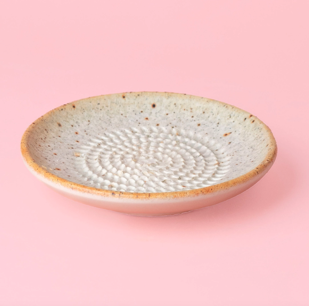 PRATO RALADOR PEQUENO "BEGE-AREIA" ALFAR TIERRA COCIDA Prato raso cerâmico creme com padrão circular e borda amarela sobre fundo rosa