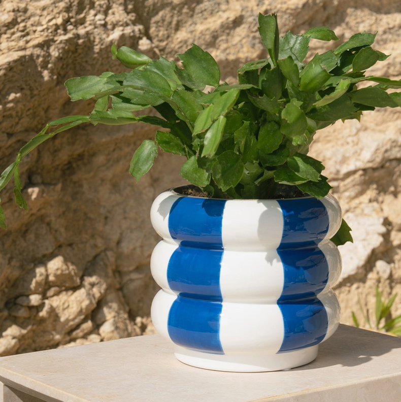 VASO EM CERÂMICA AZUL EM FORMA DE BOIAS EMPILHADAS BALVI Vaso cerâmico azul e branco com planta verde num fundo de parede de pedra