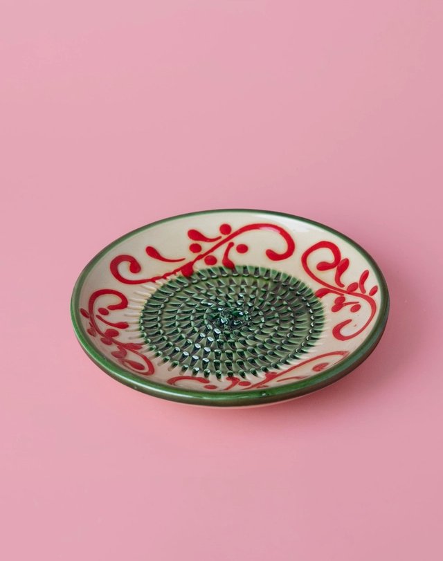 PRATO RALADOR PEQUENO "VERDE ALHAMBRA" ALFAR TIERRA COCIDA Prato cerâmico decorativo circular com padrão verde e vermelho sobre fundo rosa.