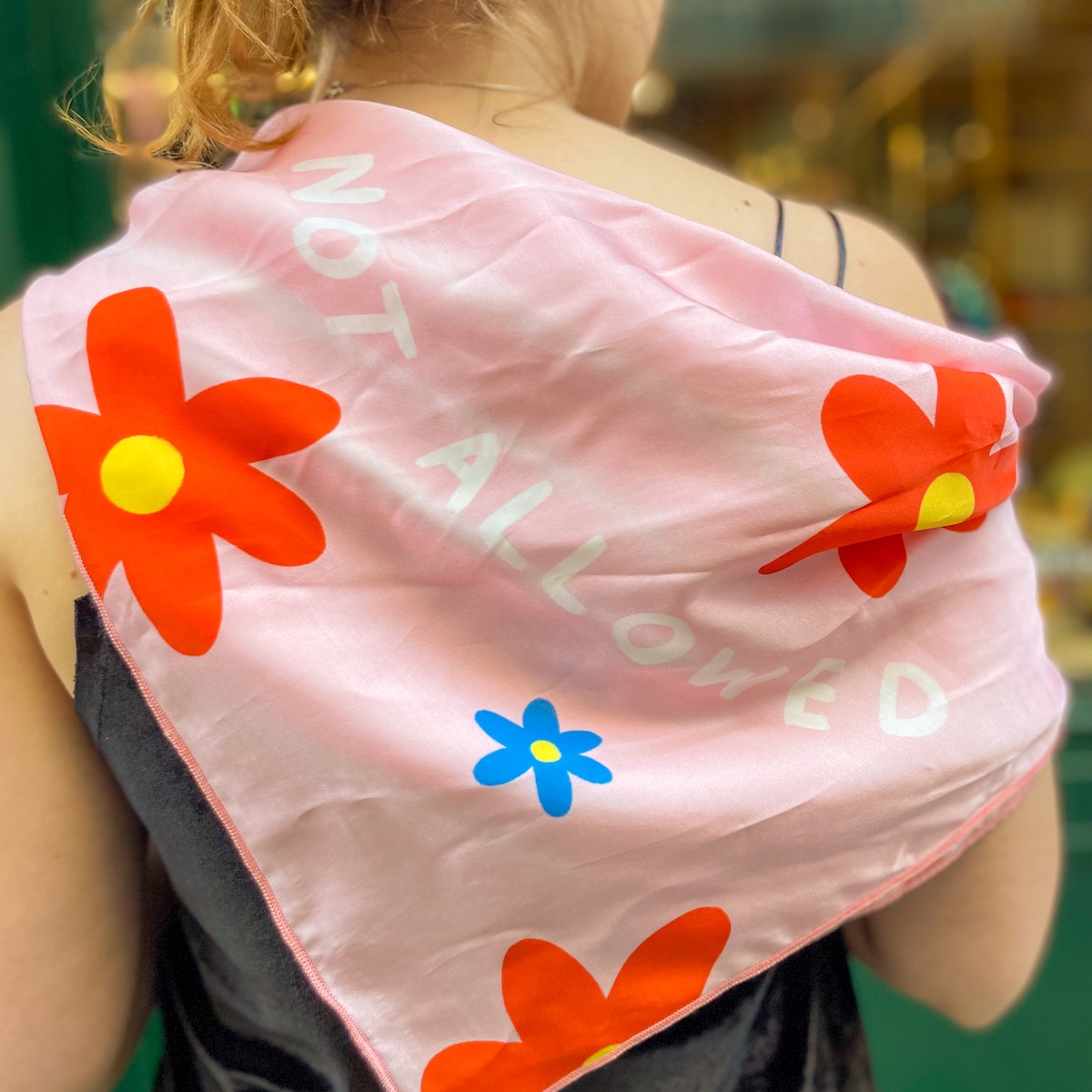 LENÇO "MESSY" KIKA Lenço rosa com flores laranjas e uma azul, texto branco 'NOT ALLOWED' e mulher com roupa preta vista de costas